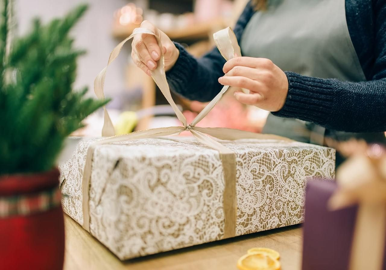 A person in an apron ties a ribbon on a white lace-patterned gift box.